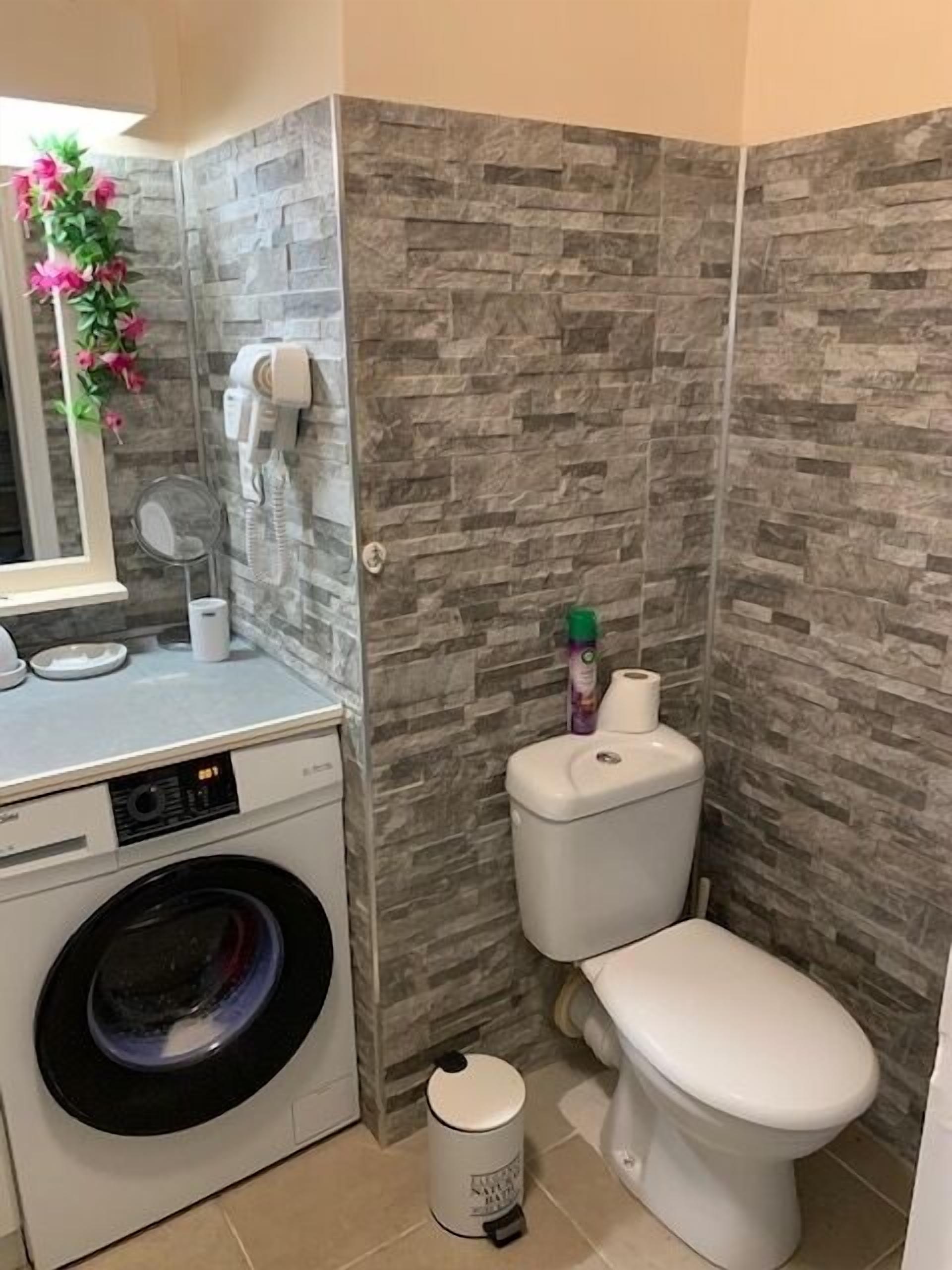 A compact bathroom with a washing machine, toilet, and a mirror.