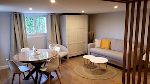 A modern living room with a round dining table, two white chairs, a sofa with a yellow pillow, and a large wardrobe.