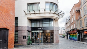 Fachada de hotel con diseño curvo, grandes ventanales de vidrio y un letrero que dice "NYX HOTEL".