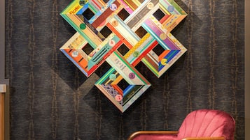 A red velvet armchair and a black side table in a room with a textured wall and a colorful geometric wall art piece.