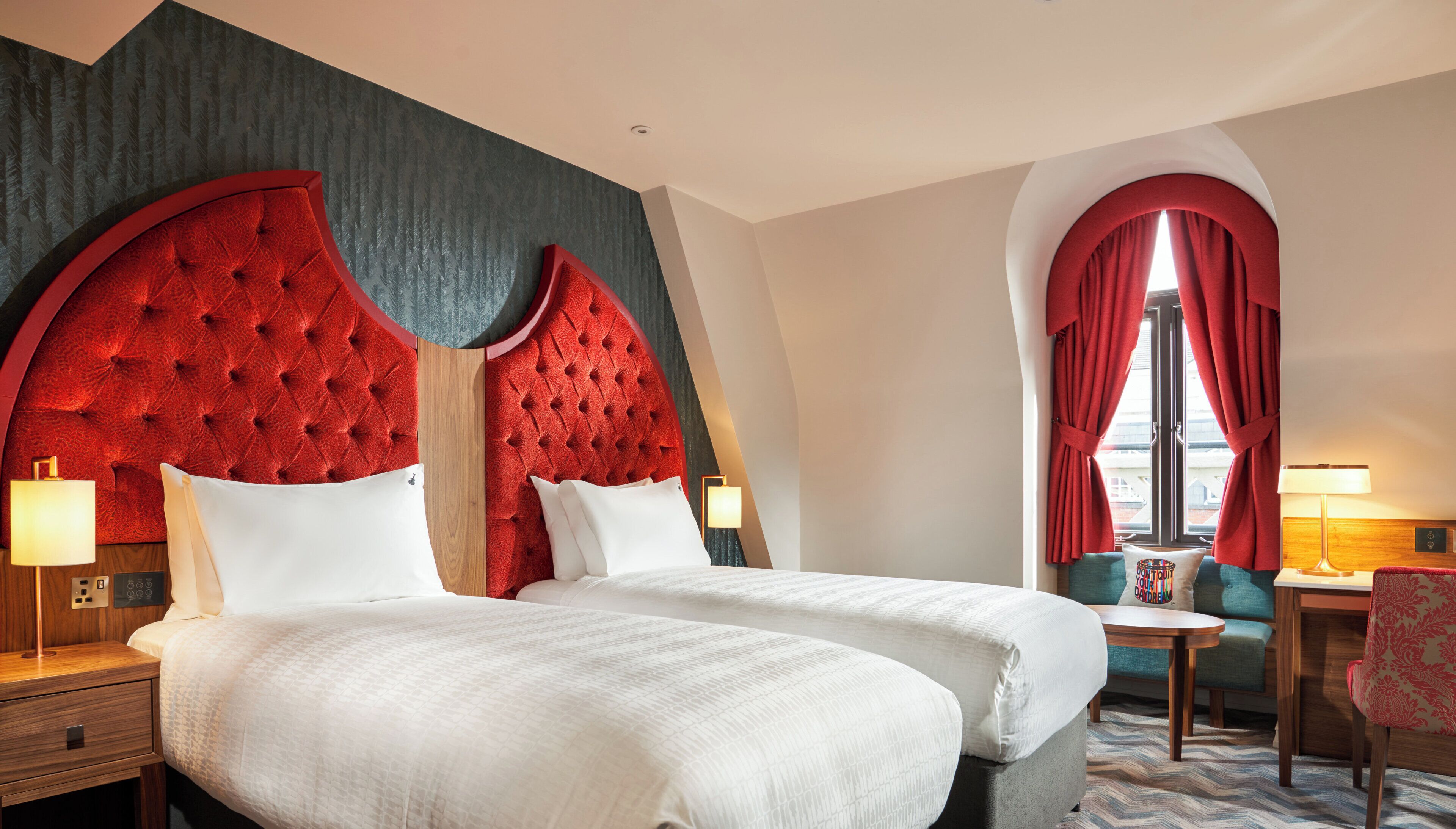 Habitación de hotel con dos camas, zona de estar con una mesa y sillas, y ventana con cortinas.