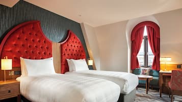 Habitación de hotel con dos camas, zona de estar con una mesa y sillas, y ventana con cortinas.