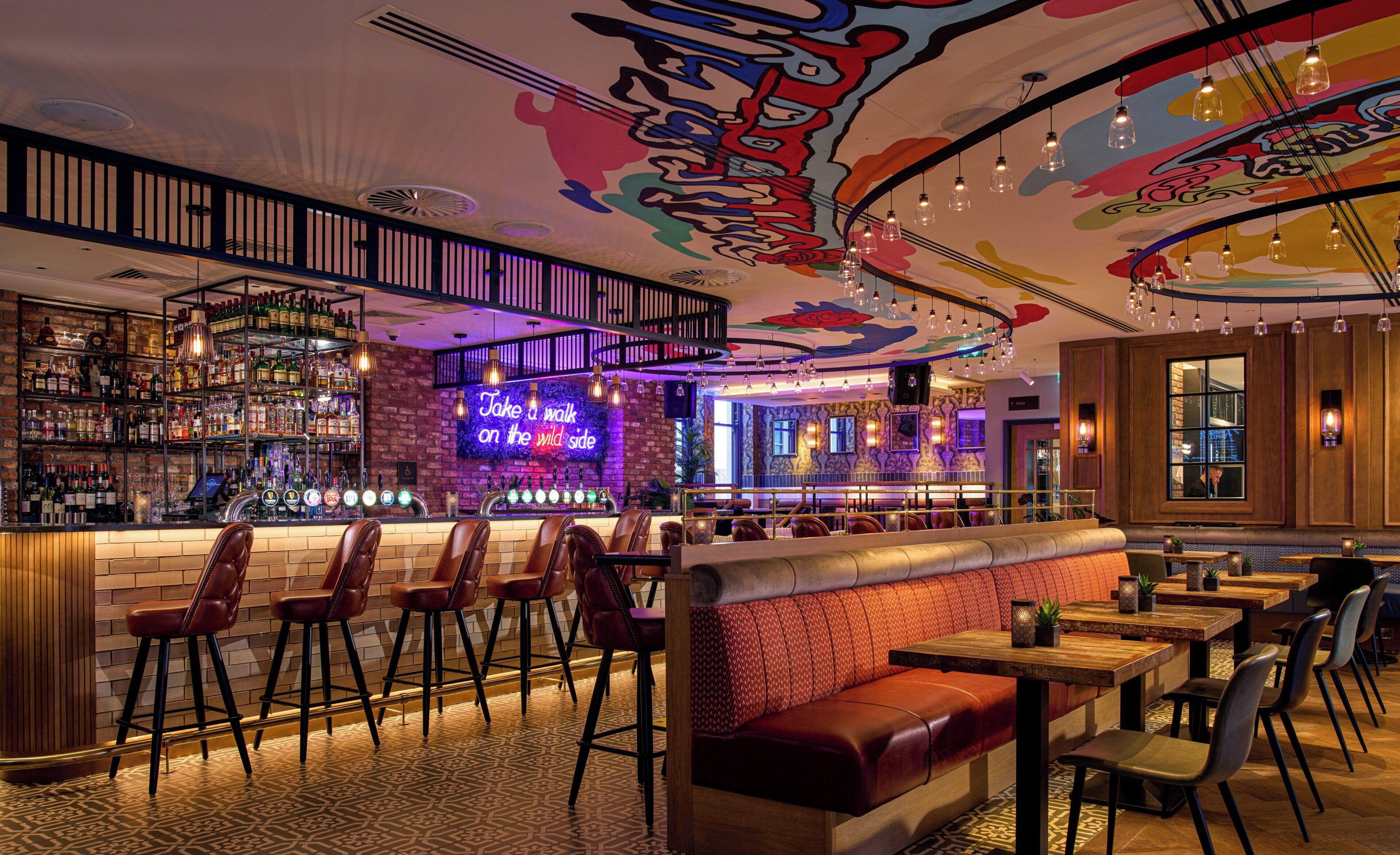 A bar area with a neon sign, leather seating, and a patterned floor.