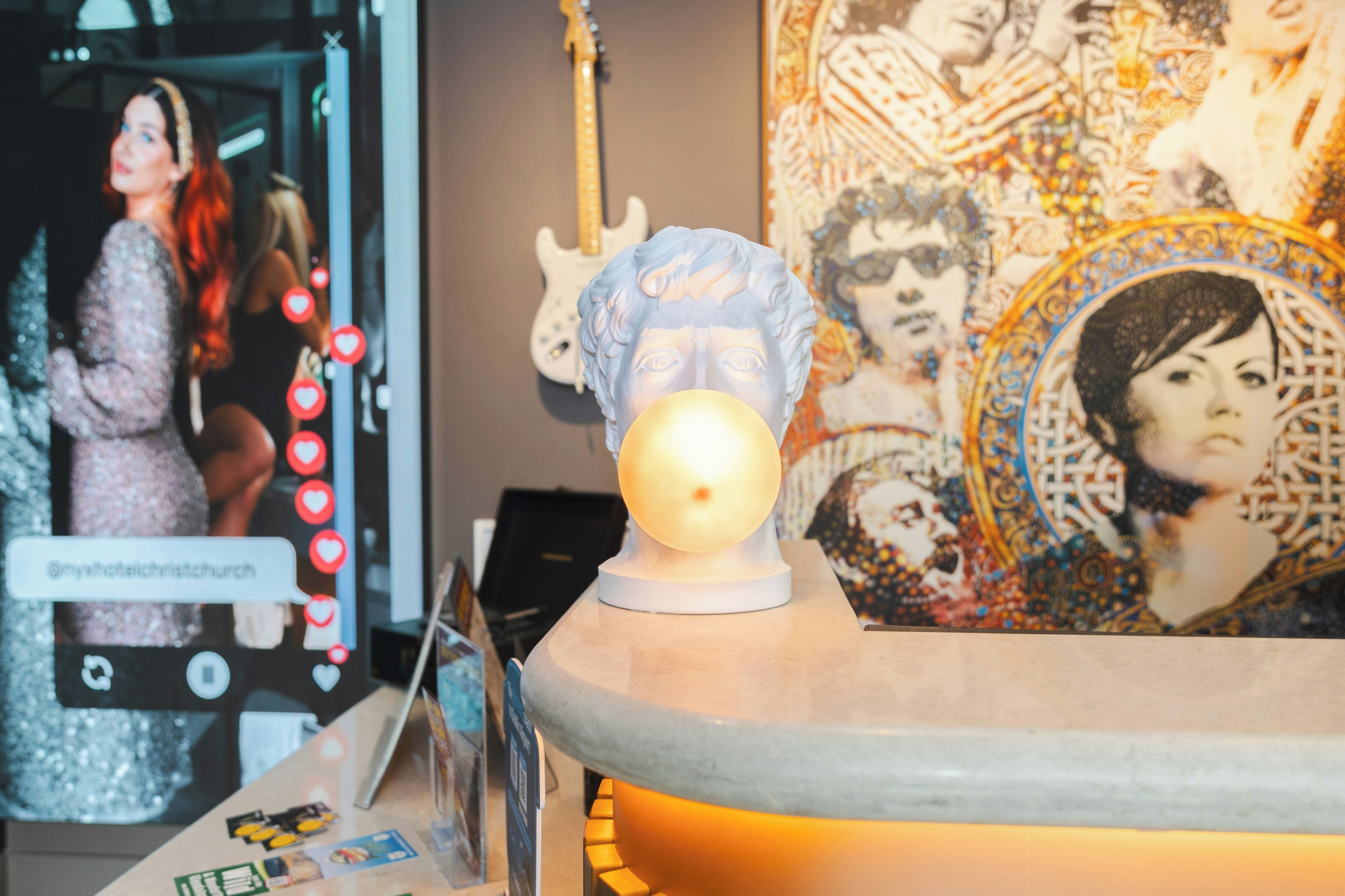 Una habitación con una lámpara decorativa, una guitarra y un cartel con el retrato de una mujer.