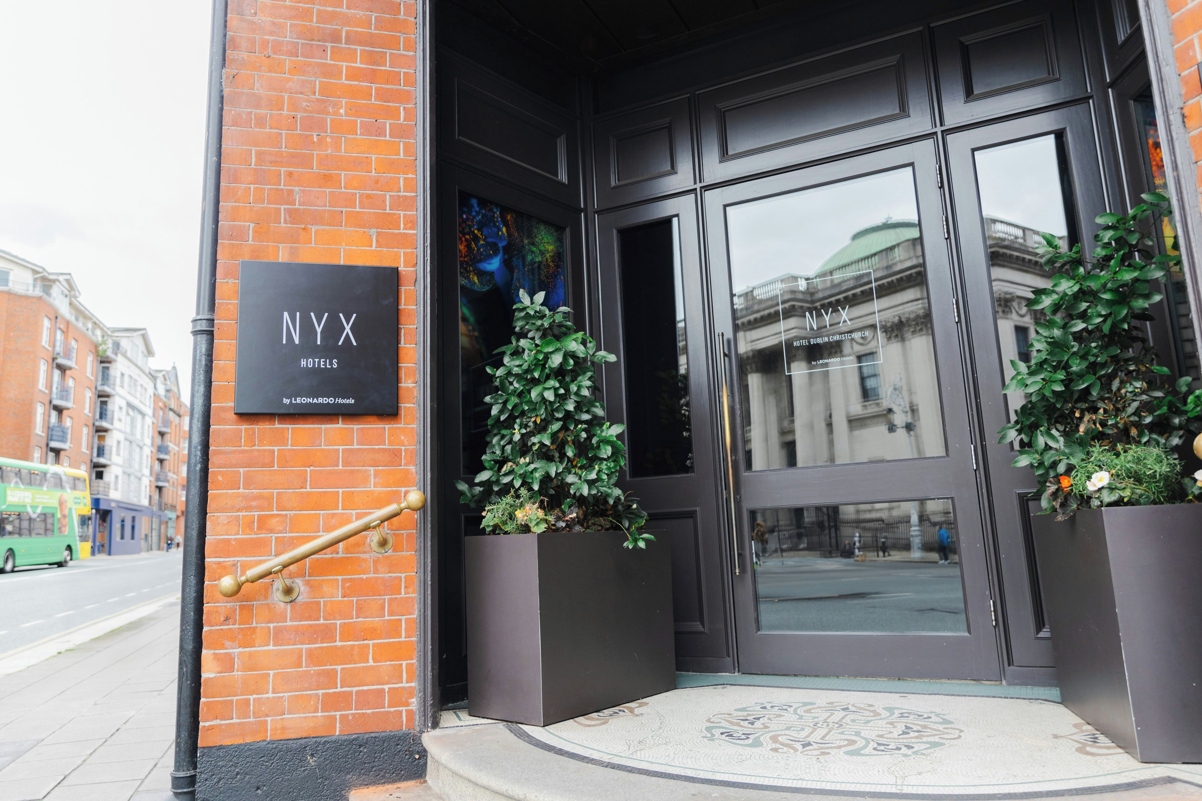 The entrance to NYX Hotels with a black signboard, a glass door, and potted plants.