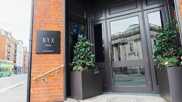 The entrance to NYX Hotels with a black signboard, a glass door, and potted plants.