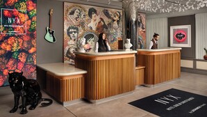 Zona de recepción de hotel con un mostrador de madera, una escultura de un gato negro y un mural colorido.