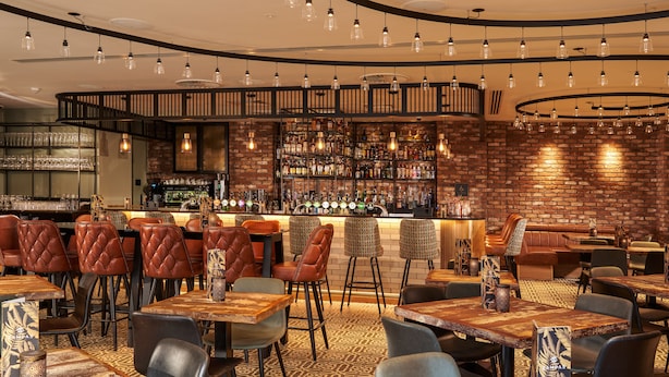 Zona de bar con pared de ladrillo, diversas opciones de asientos como cabinas y mesas, y una variedad de taburetes.