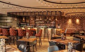 Zona de bar con pared de ladrillo, diversas opciones de asientos como cabinas y mesas, y una variedad de taburetes.