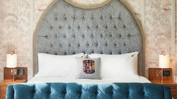 A bedroom with a tufted headboard, a bed with white linens, a blue patterned bedspread, and two bedside tables with lamps.