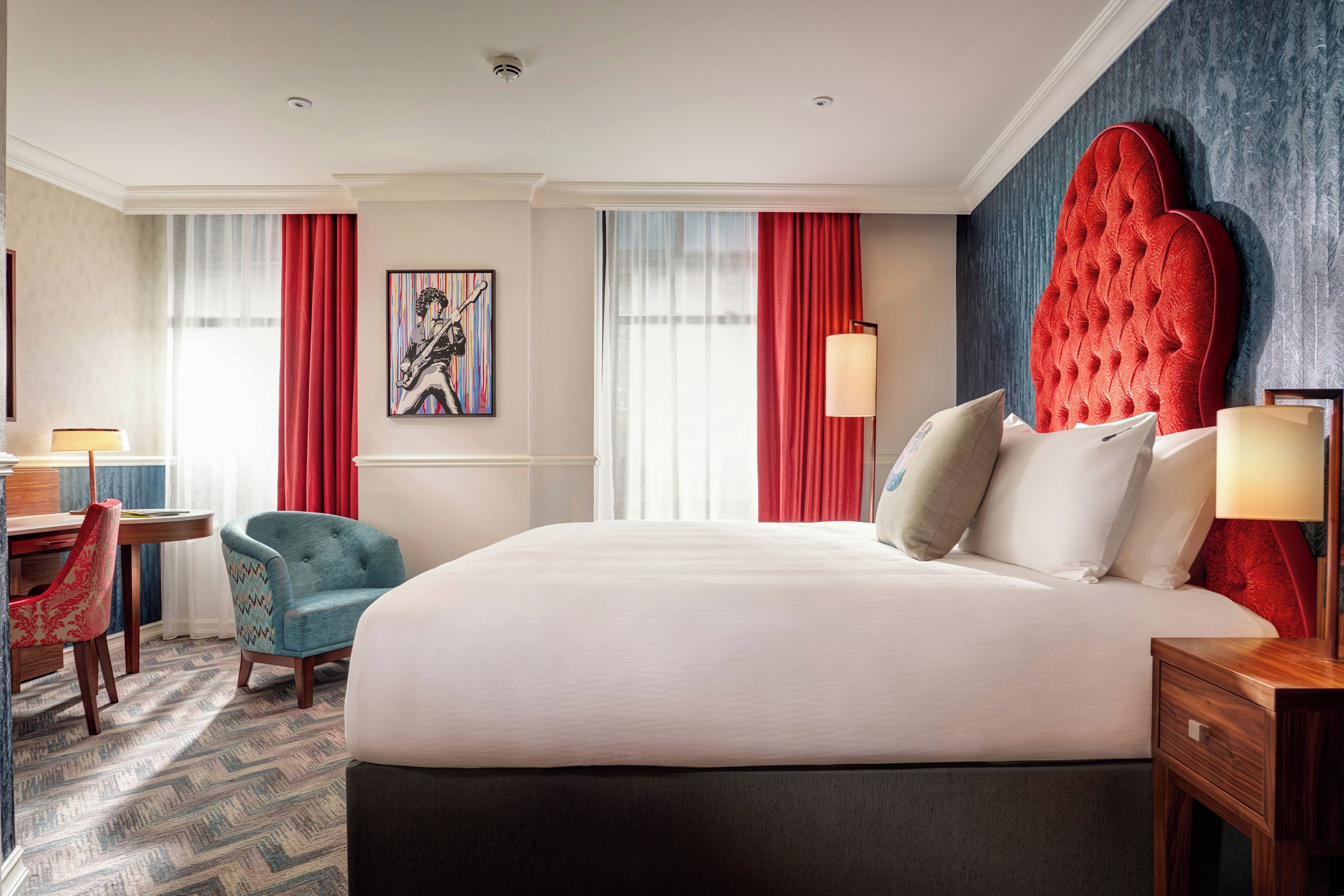 A hotel room with a large bed, a desk, a chair, and a painting on the wall.