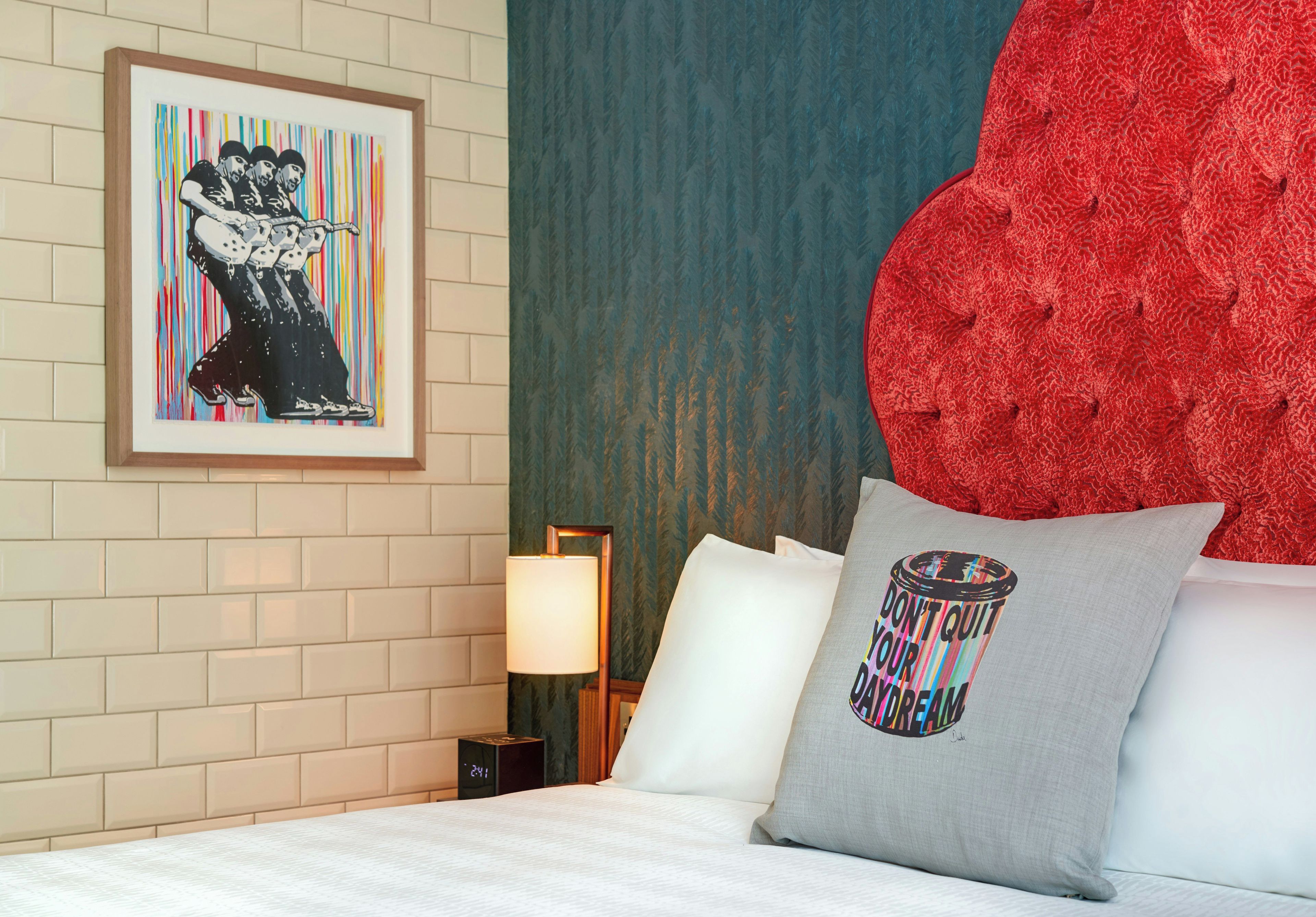 A hotel room with a bed, pillows, a framed artwork, a lamp, and a large red decorative piece.
