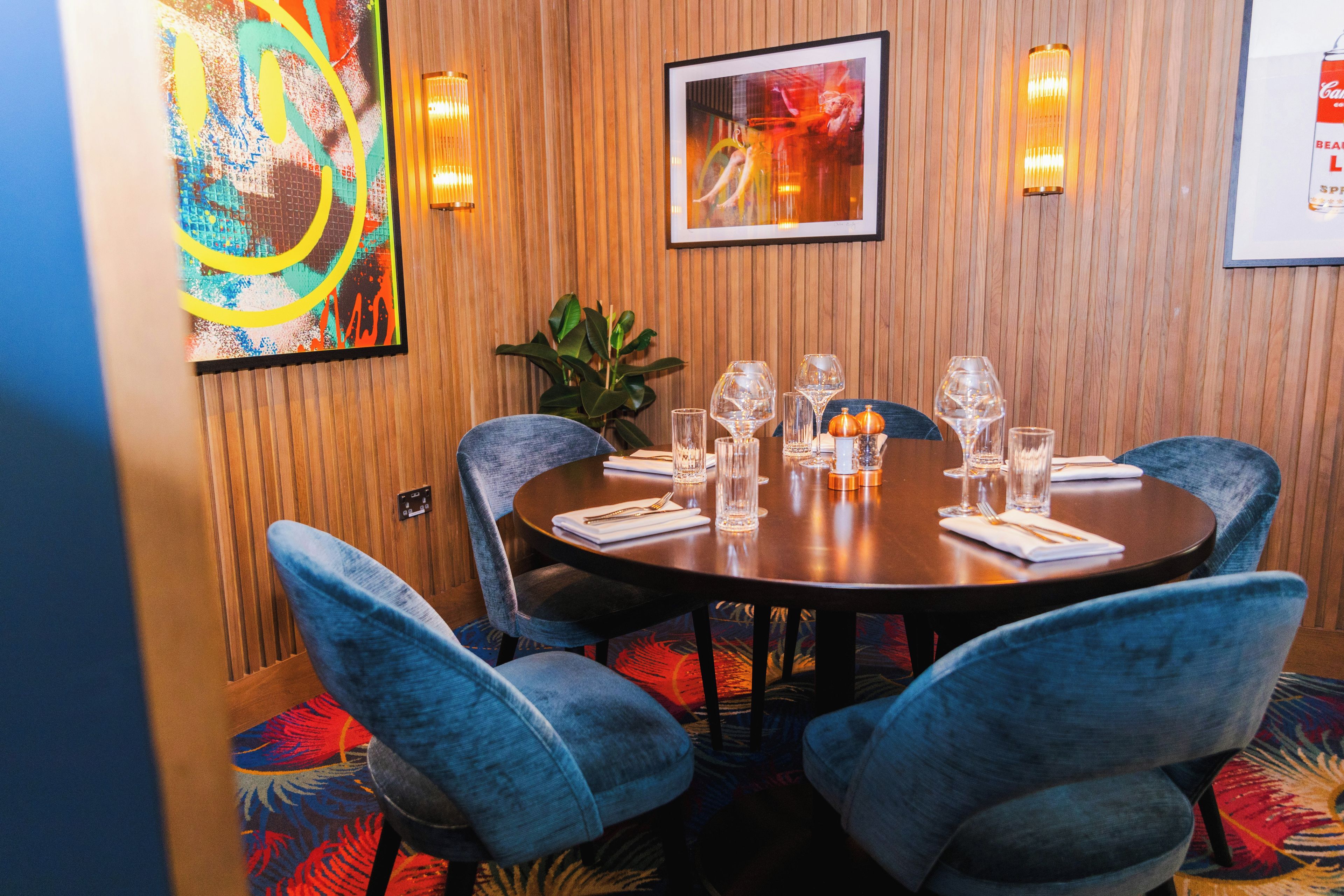 A dining area with a round table set for four, surrounded by blue upholstered chairs.