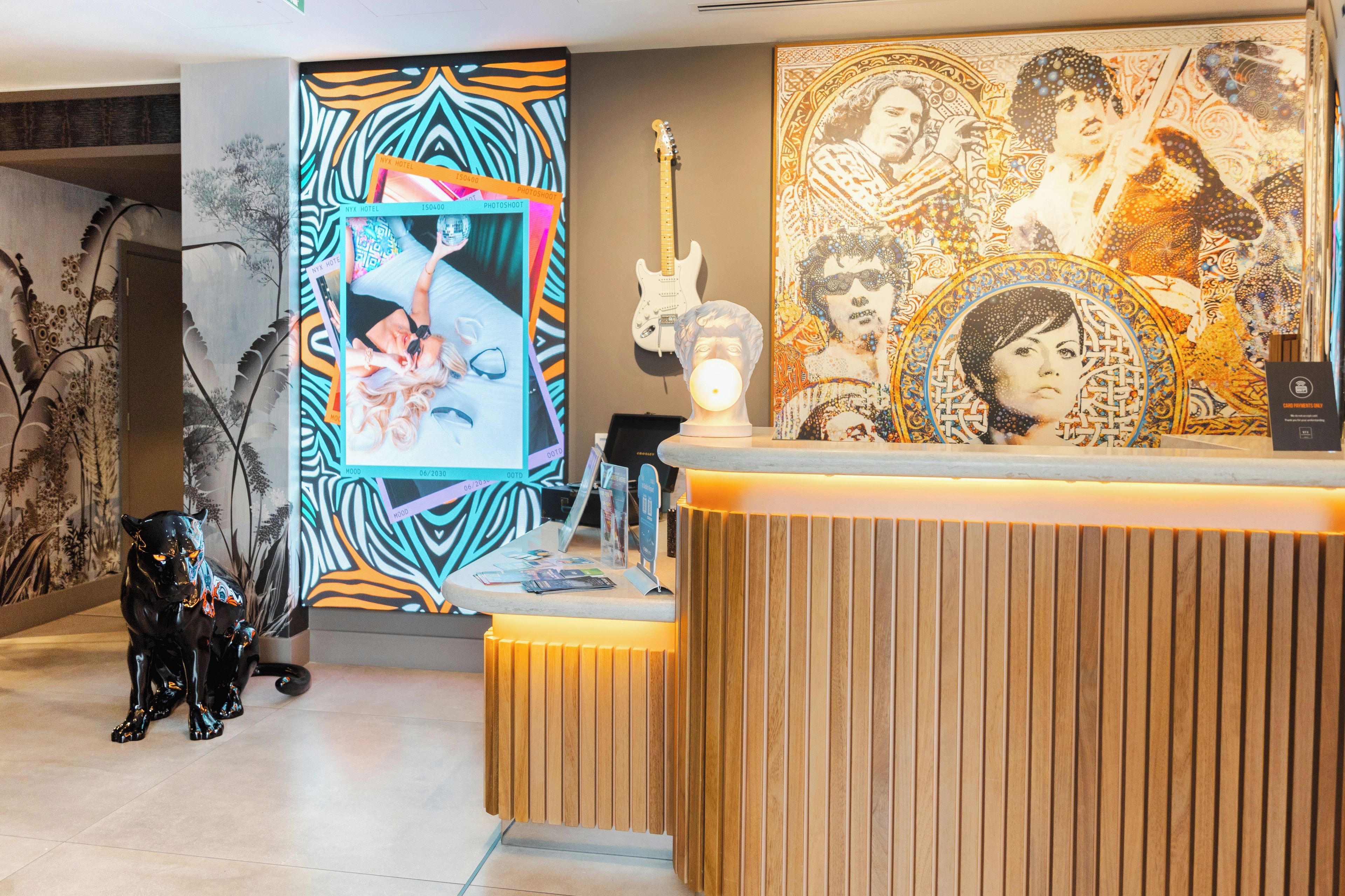 Un espace d’accueil d’hôtel au design moderne, comprenant un comptoir d’accueil en bois, une grande peinture abstraite et une statue de panthère noire.