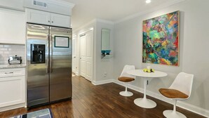 A modern kitchen with white cabinetry, stainless steel appliances, and a dining area with two white chairs and a table. - Garden Apartment with Parking, Heated Pool Access (Savannah)