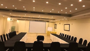 Ein Konferenzraum mit einem langen Tisch, Stühlen, einer Projektorleinwand und einer Whiteboard-Tafel.