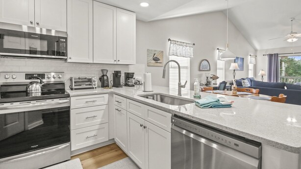 A modern kitchen with white cabinets, stainless steel appliances, and a large island with a dishwasher. - Pawleys Island Condo with Golf Views  Minutes to beach Pool/Hot Tub Dog-friendly (Pawleys Island)