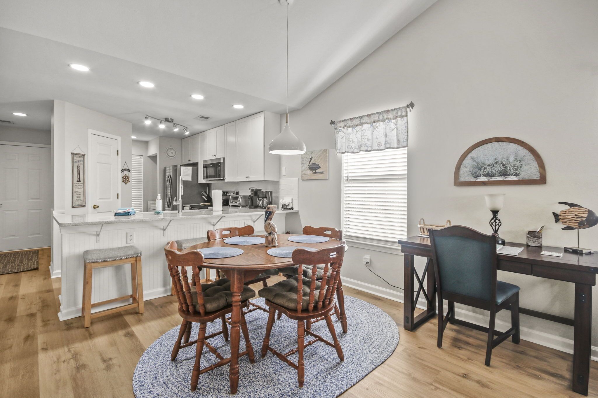 A modern kitchen with white cabinets, a central island, and a dining area with a round table and chairs.