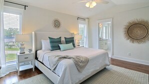 Quarto com cama, mesas de cabeceira, ventilador no teto e vista para o exterior.