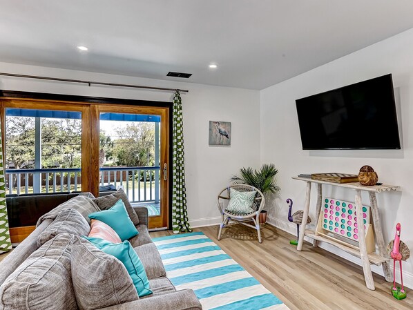 A living room with a sofa, a television, a wooden table, and a view through a glass door. - Heated Pool Access | 5*Clean | Flex Cancelation (Tybee Island)