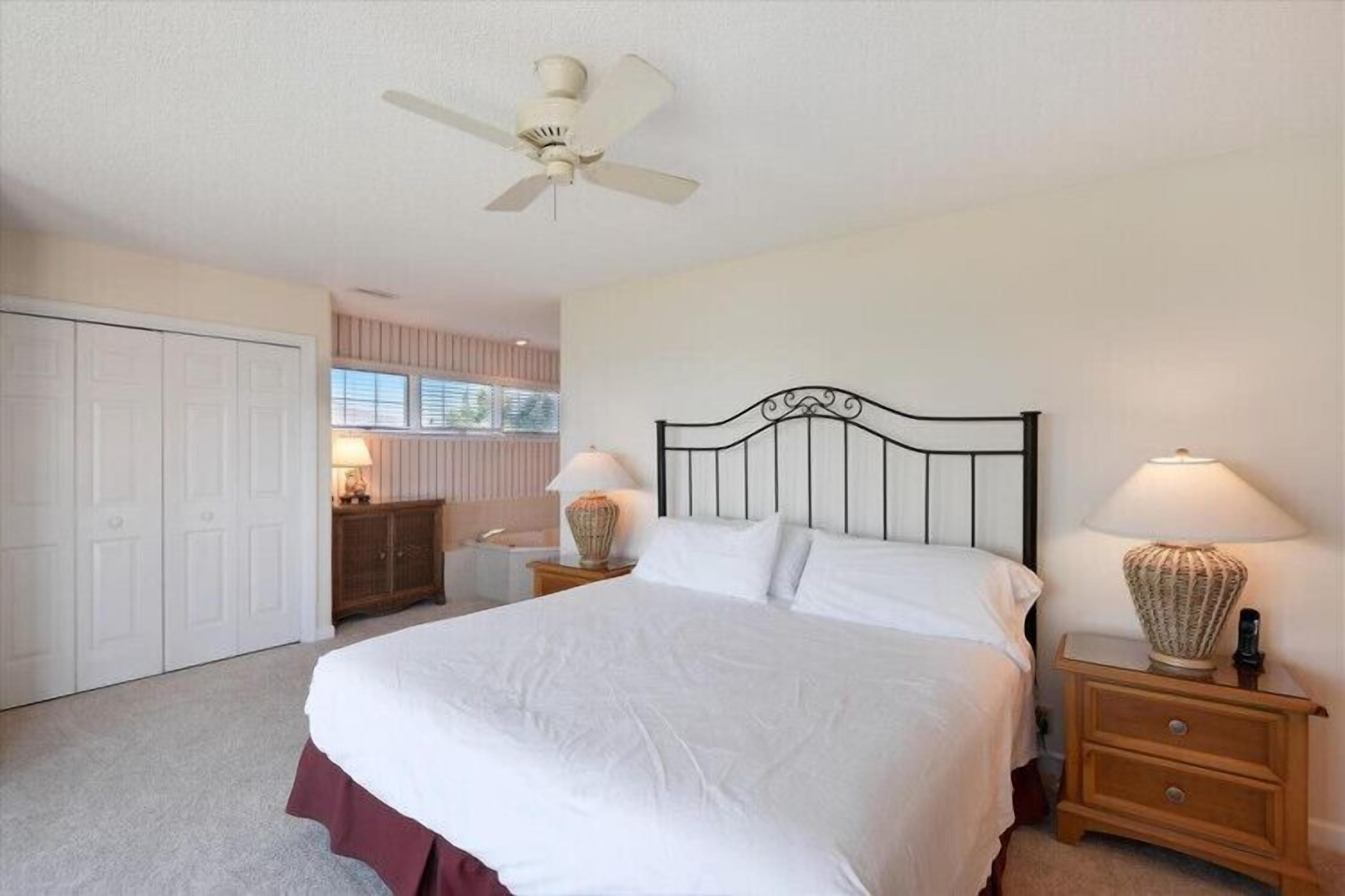 A bedroom with a bed, bedside tables, a ceiling fan, a wardrobe, and a window.