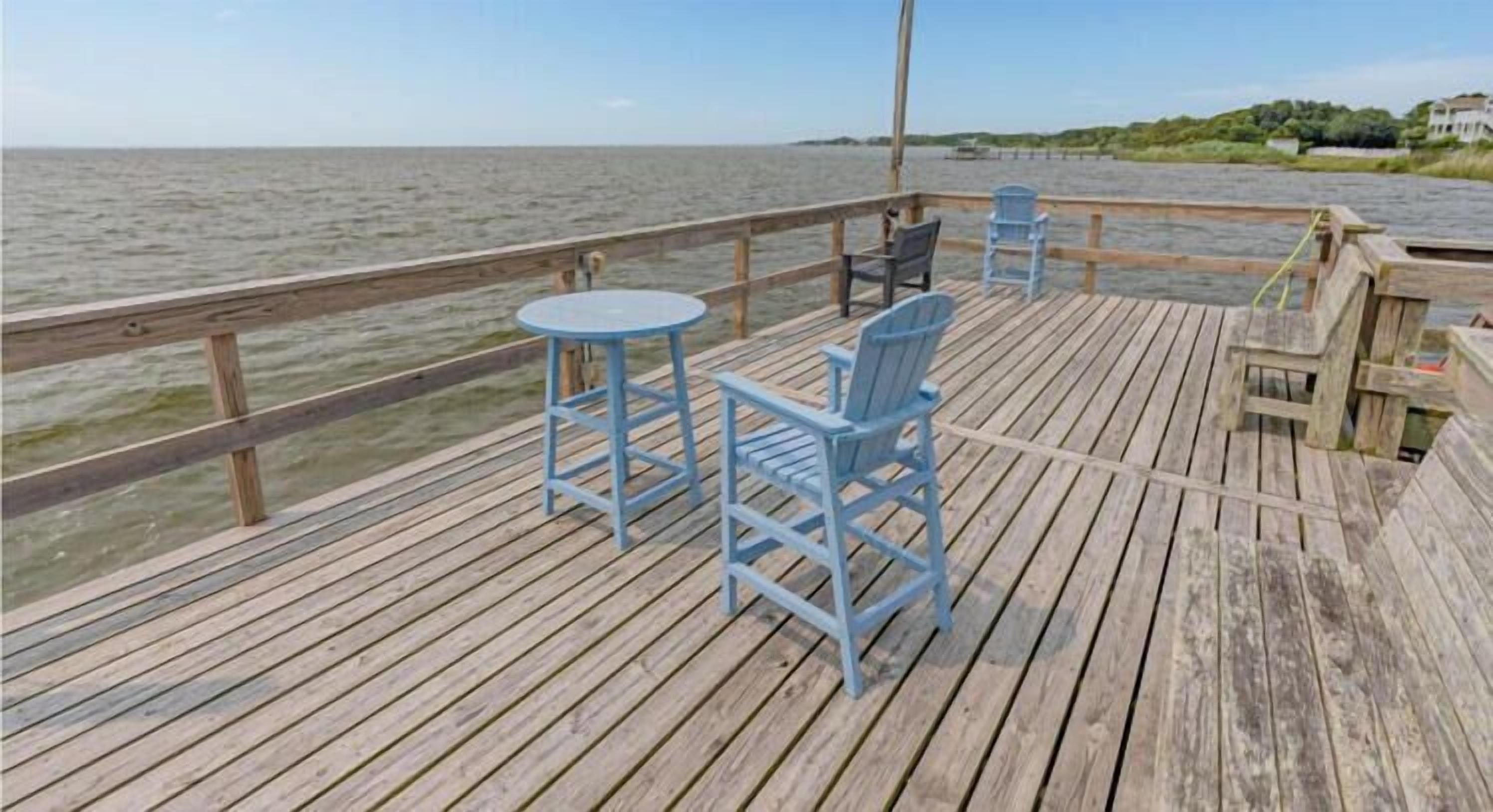 A wooden deck with a table and chairs, overlooking a body of water.