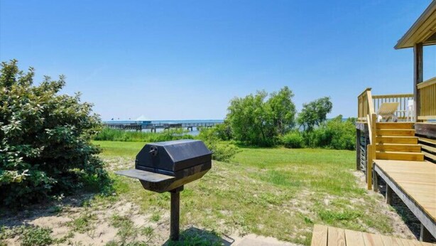 A barbecue grill in a grassy area with a wooden deck and a view of the water. - The Tayer-Soundfront at Ships Watch in Duck (Duck)