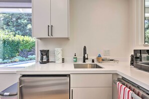 Une cuisine moderne dotée d’appareils électroménagers en acier inoxydable, d’un plan de travail blanc et d’une fenêtre donnant sur un paysage verdoyant.