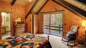A bedroom with a wooden ceiling, a bed with a quilt, a rocking chair, a dresser, and a window with a view of trees. - Community Perks: Retreat w/ Thirteenth Lake Access (North River)