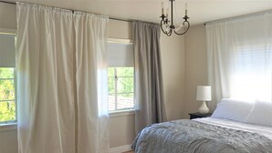 Une chambre à coucher avec un lit, une table de chevet, une lampe et une fenêtre avec des rideaux.