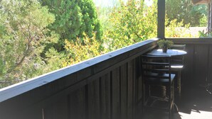 Une terrasse en bois avec une table et des chaises, donnant sur un jardin agrémenté de divers arbres et arbustes.