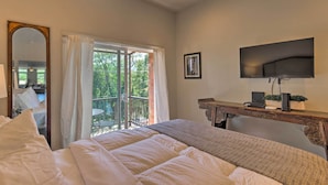 Een slaapkamer met een groot bed, een aan de muur bevestigde televisie en een balkon met uitzicht op groen.
