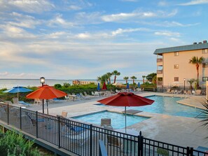A pool area with lounge chairs and umbrellas, a view of the ocean, and a building with balconies. - Beachside Condo with Great Location (Tybee Island)
