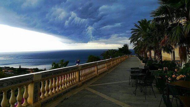 Un balcón frente al mar con vistas al océano, palmeras y mobiliario exterior.