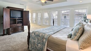 Quarto com uma cama grande, uma televisão sobre um móvel de madeira e um ventilador de teto.