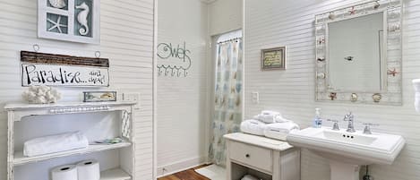 A bathroom with a vanity, a mirror with decorative elements, and a shelf with towels and toiletries.