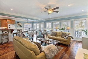 A spacious living room with a high ceiling fan, wooden flooring, and large windows with blinds. - Beach Home, Private Boardwalk, Oceanviews (Tybee Island)