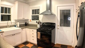 A kitchen with white cabinets, a black stove, and a window with blinds.