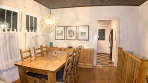 A dining area with a wooden table and chairs, a hanging light fixture, and framed pictures on the wall.