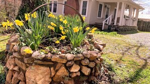 A stone planter with yellow flowers in front of a house with a porch and a brick chimney.