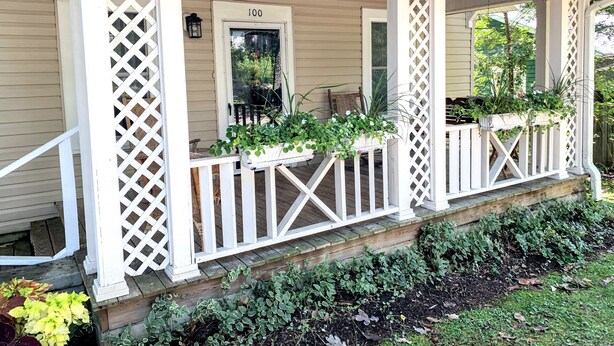 A covered porch with white lattice railings, a door labeled "100", and potted plants.