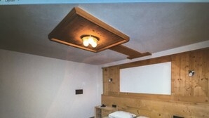 Un dormitorio con techo de madera, una cama con ropa de cama floral, una mesita de noche y un aparador.