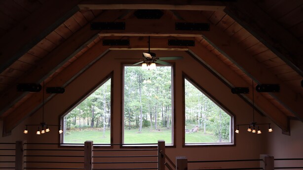 Una habitación con techo inclinado, un ventanal con vistas a un bosque y una escalera con barandilla.