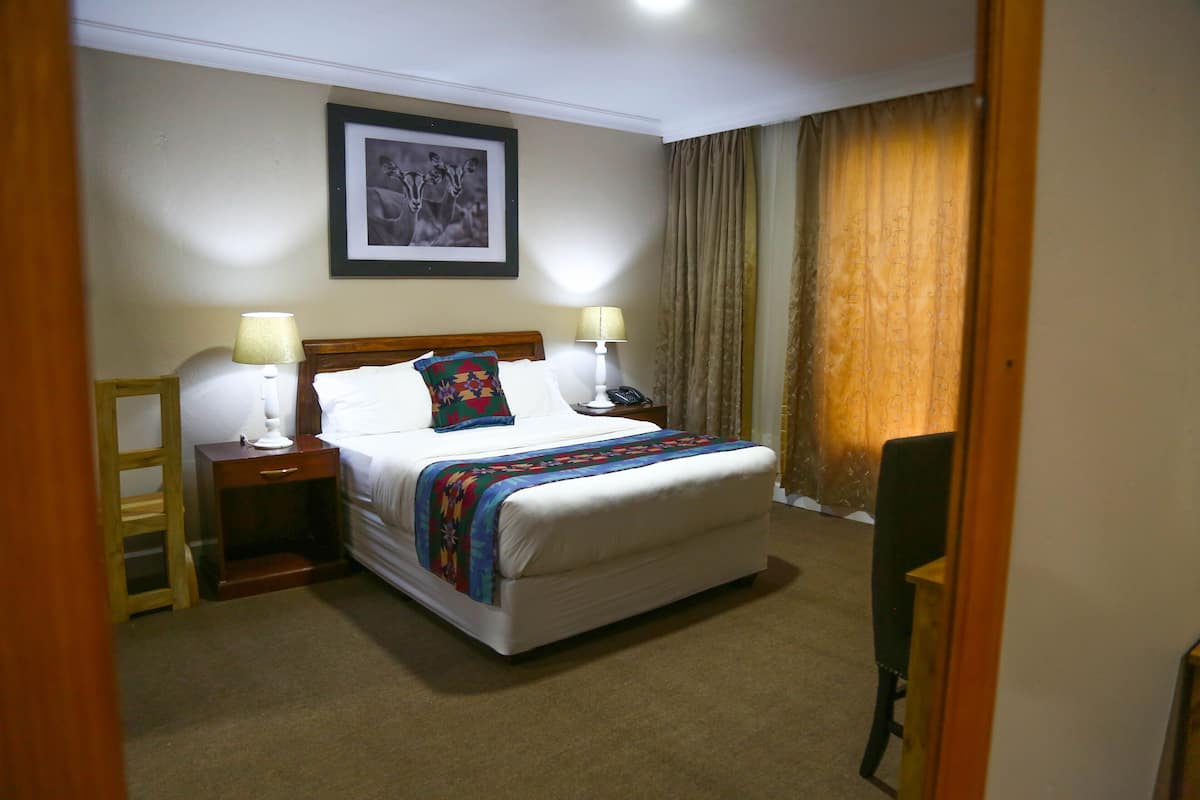 A hotel room with a bed, bedside tables, a lamp, a framed picture on the wall, and a curtain.