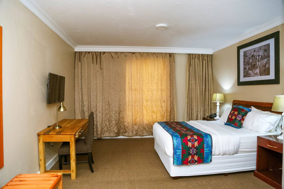 A hotel room with a bed, a desk, a chair, a television, and a painting on the wall.