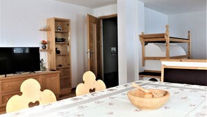 A room with a television, wooden furniture, a table with a floral tablecloth, and a bunk bed. - Apartment Weisse Zinne (St.Johann)