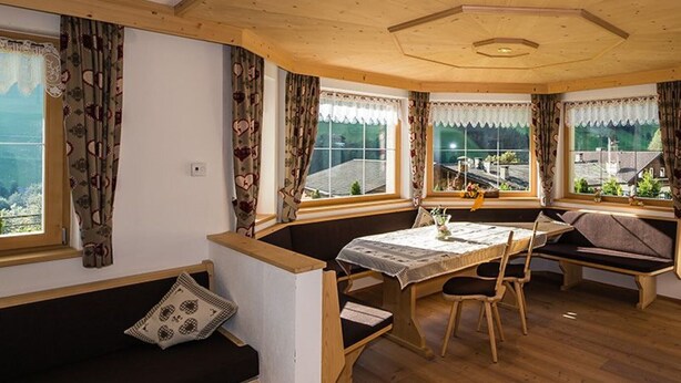 A cozy room with a wooden ceiling, a dining table with chairs, a bench, and large windows with curtains. - Apartment Weisse Zinne (St.Johann)