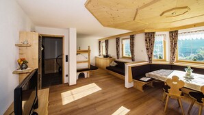 A cozy room with wooden floors, a built-in bench, a table with a floral centerpiece, and a window with curtains. - Apartment Weisse Zinne (St.Johann)