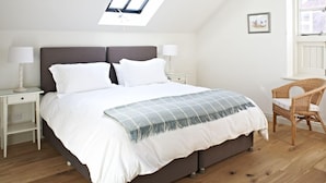 A bedroom with a bed, two bedside tables, a chair, a skylight, and a window. - Manor Farm Courtyard Cottages (Thatcham)