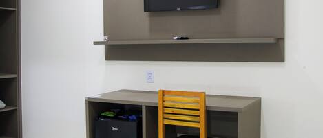 A room with a bed, a desk, a chair, a television mounted on the wall, and a small refrigerator.